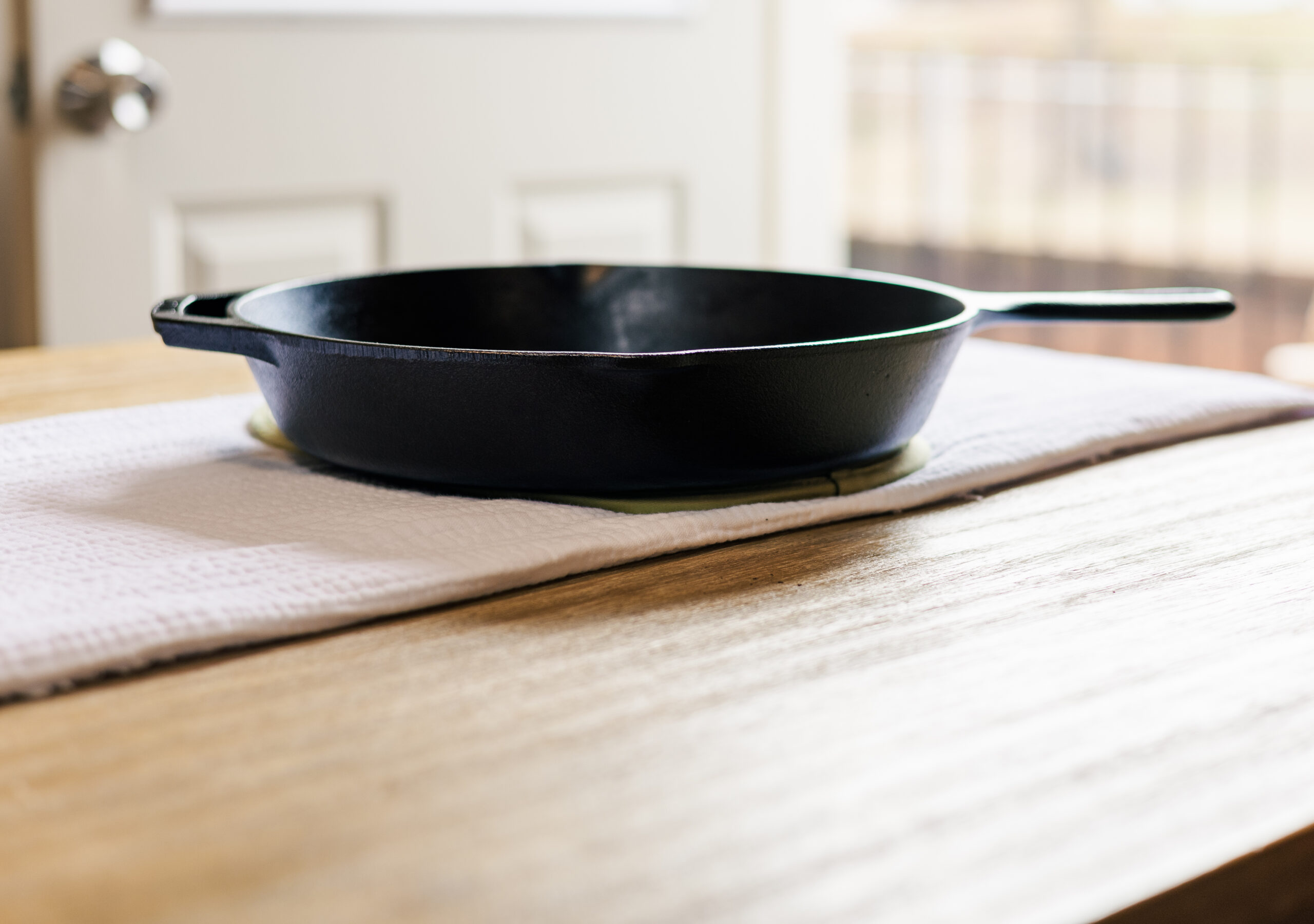 Black cast iron skillet sat on white linen on a light hard wood table, side view Photo credit: Ryan Kirst