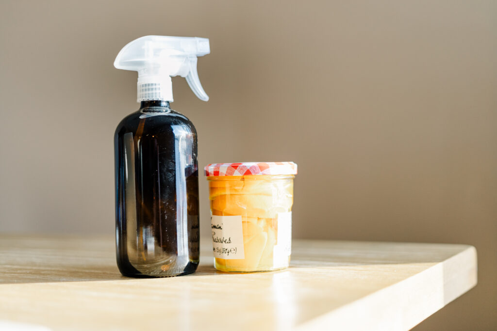 A jar of orange slices and an amber spray bottle setting on wood table in the sunlight
Photo credit: Ryan Kirst