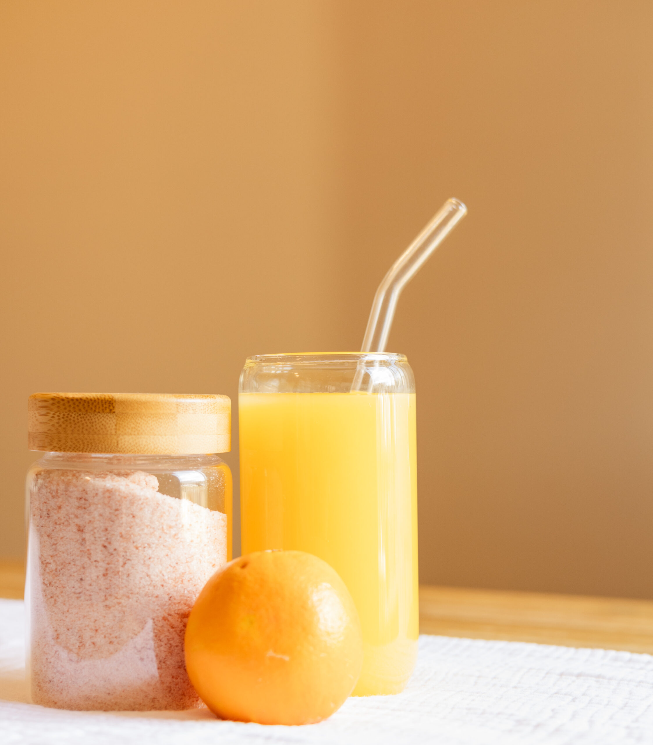 Vibrant orange drink called an adrenal cocktail in glass cup with glass straw, next to cup is an orange and a glass container of pink Himalayan salt. Photo Credit: Ryan Kirst