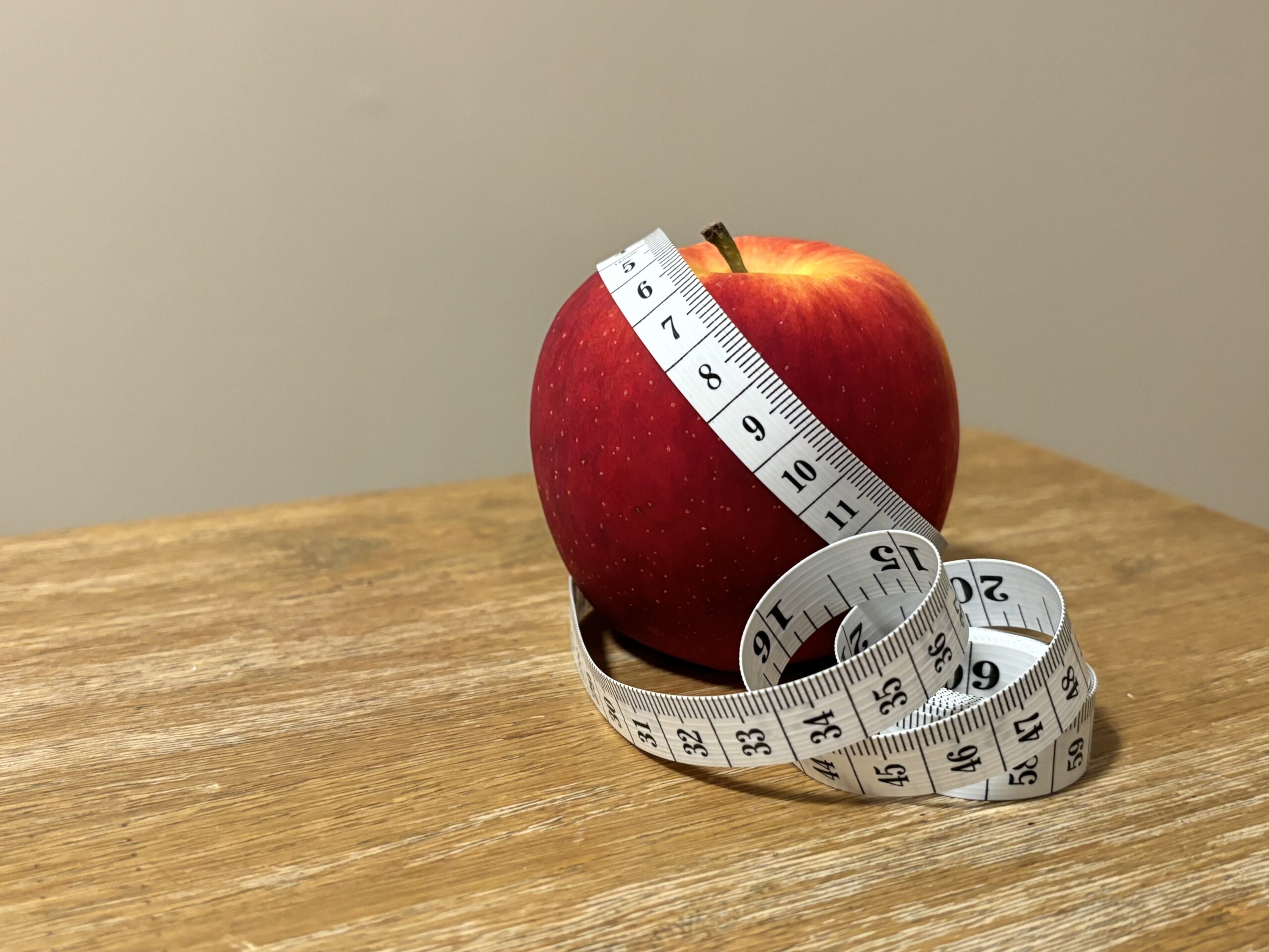 Vibrant red apple with measuring tape wrapped around it sitting on wooden table. Photo credit: Kati Kirst