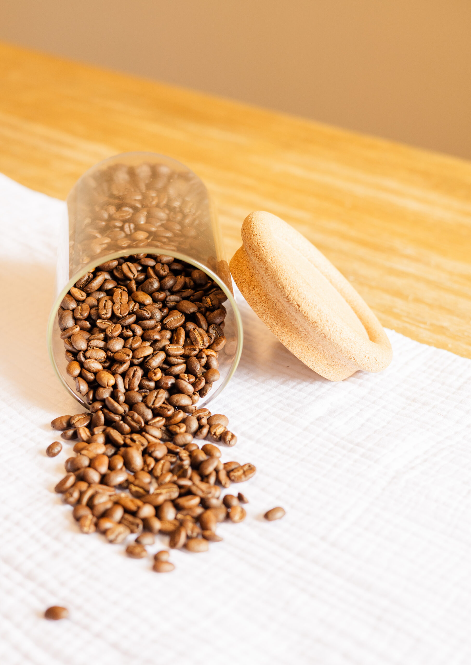 Coffee beans spilling out of glass container onto white linen cloth Photo credit: Ryan Kirst